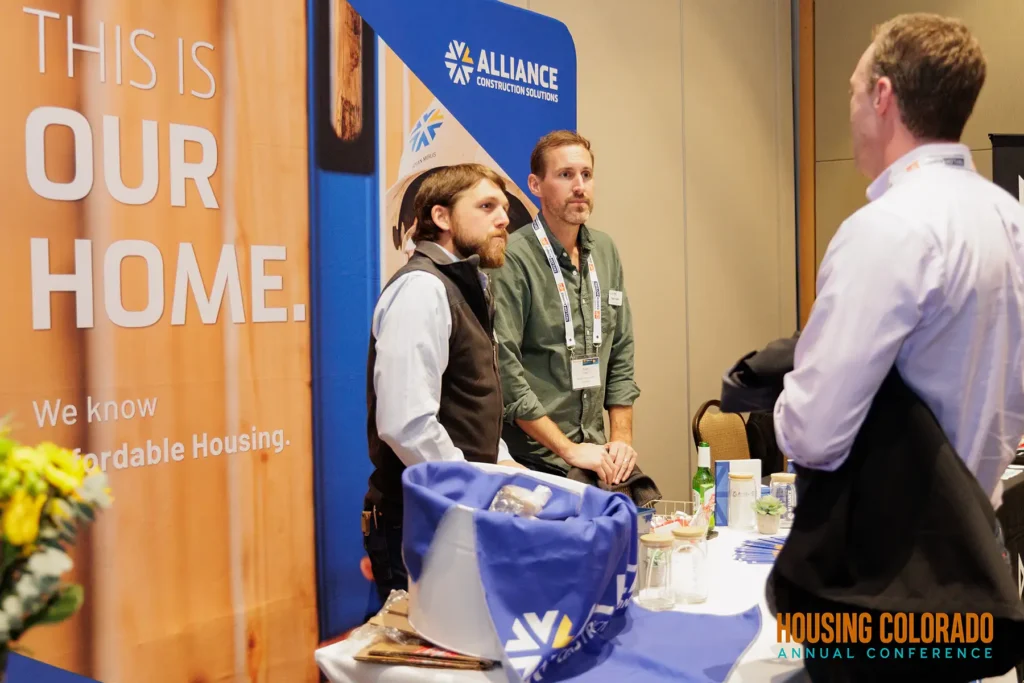 Two people from Alliance Construction Solutions talk to a man at the Housing Colorado Annual Conference