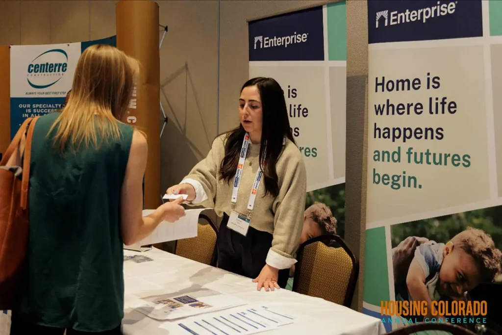 A woman hands a business card to another woman at the Housing Colorado Annual Conference